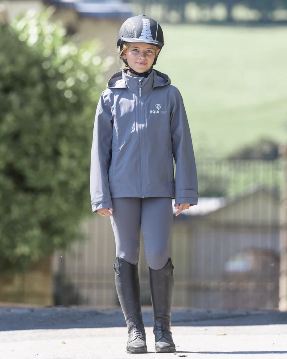 Charcoal coloured Equidry Childrens Nimbus Pack Away Jacket With Stowaway Hood on outdoor background 