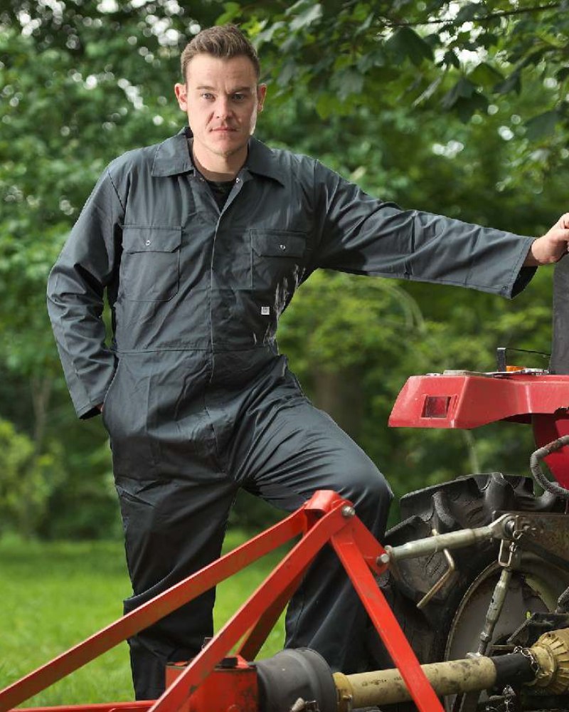 Man wearing Fort overalls beside farm machinery outdoors