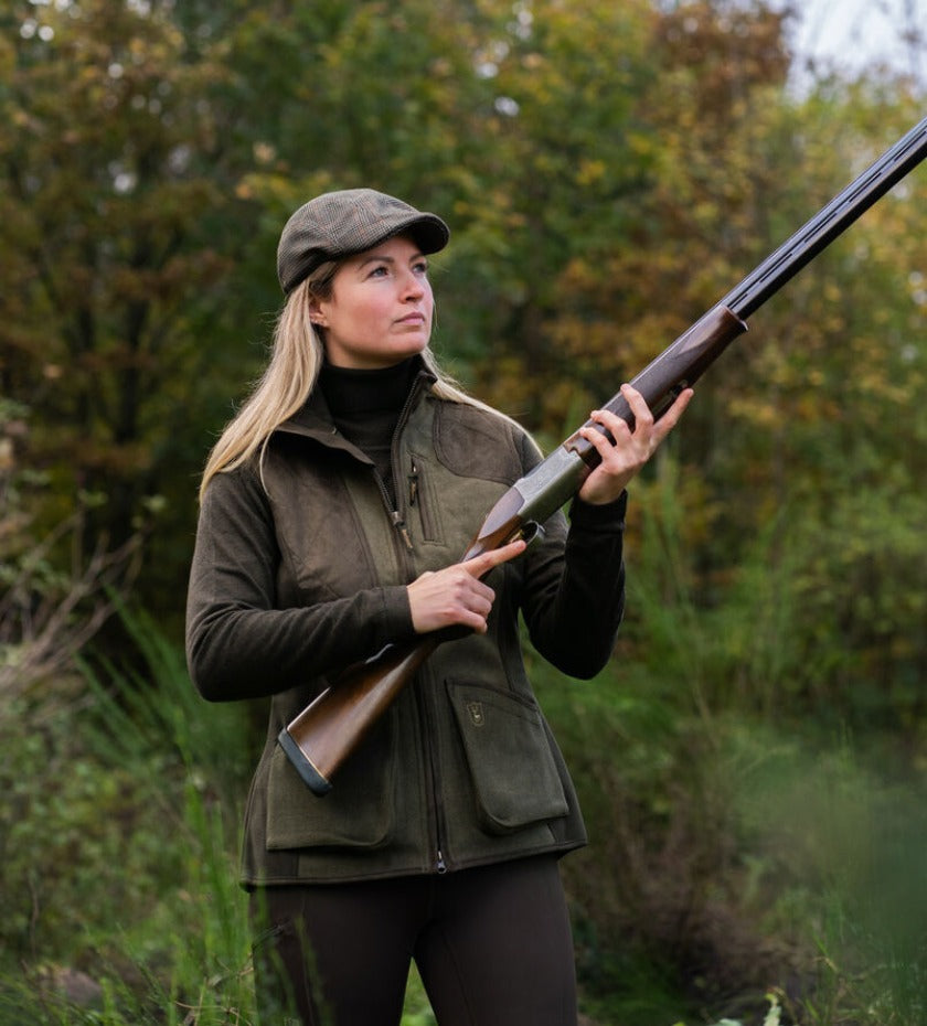 Woman wearing Deerhunter shooting clothing while holding a shotgun outdoors in countryside setting