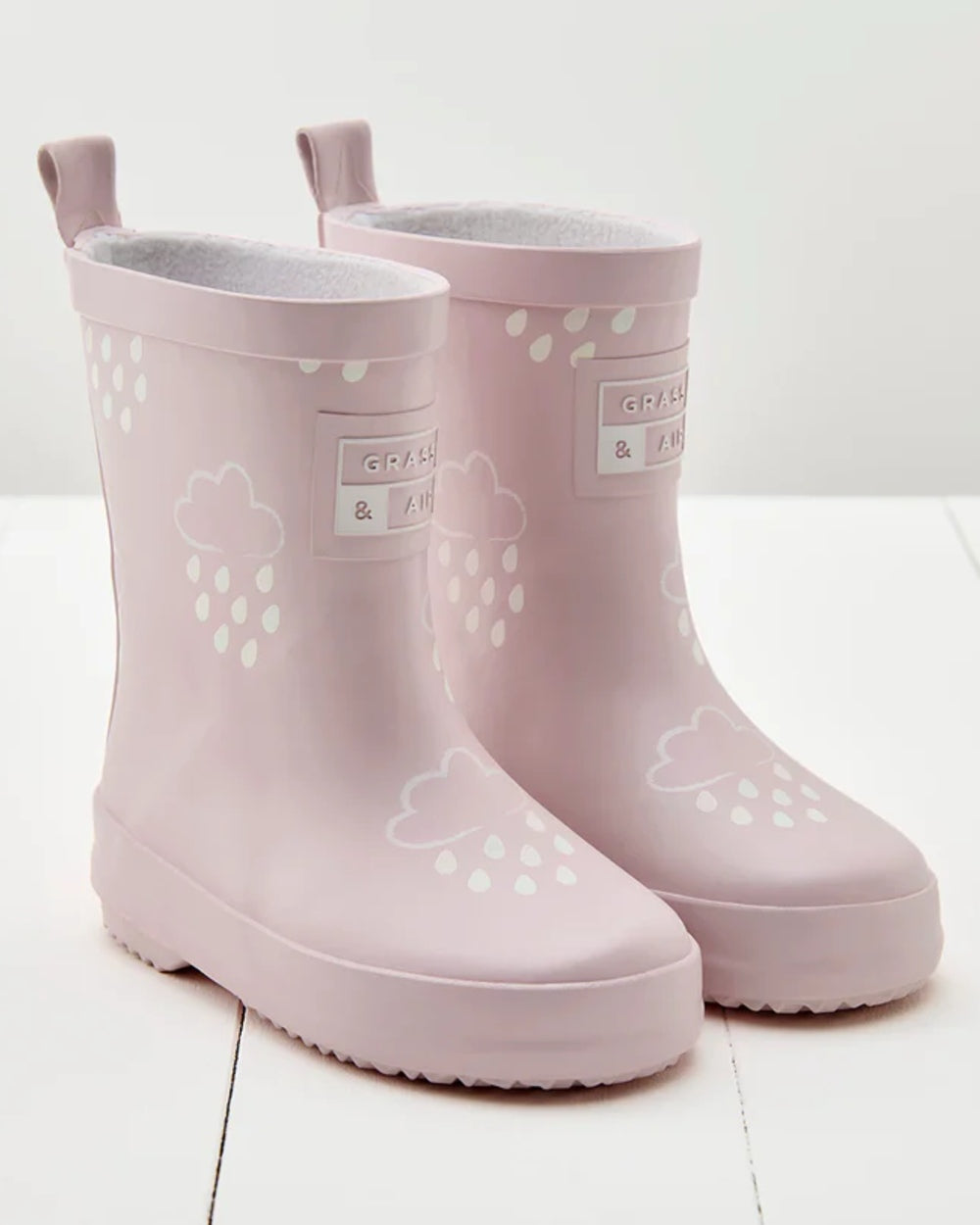 Baby Pink coloured Grass &amp; Air Childrens Colour-Revealing Wellies on wooden table background 