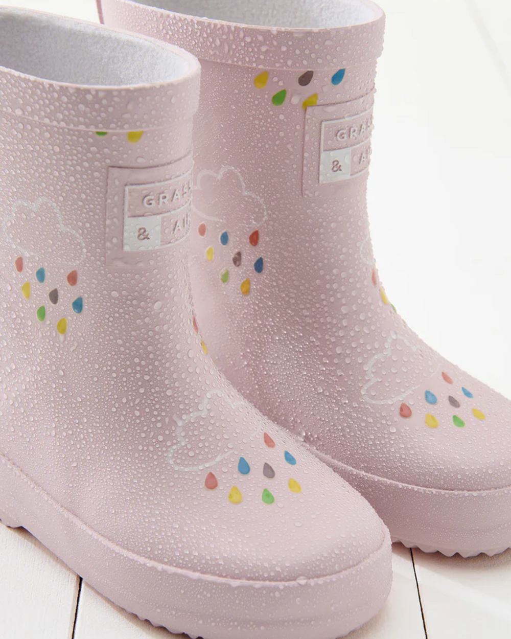 Baby Pink coloured Grass &amp; Air Childrens Colour-Revealing Wellies on wooden table background 