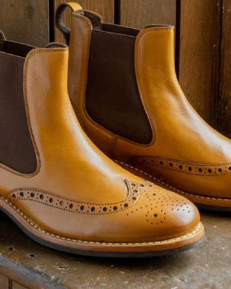 Close up image of tan Hoggs of Fife Stanley part-brogue traditional boots on a wooden bench surface. 