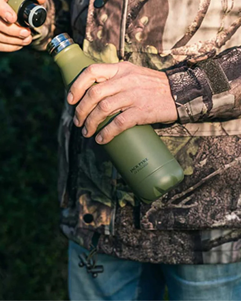 Person holding a green Jack Pyke insulated drinks bottle outdoors in camouflage clothing