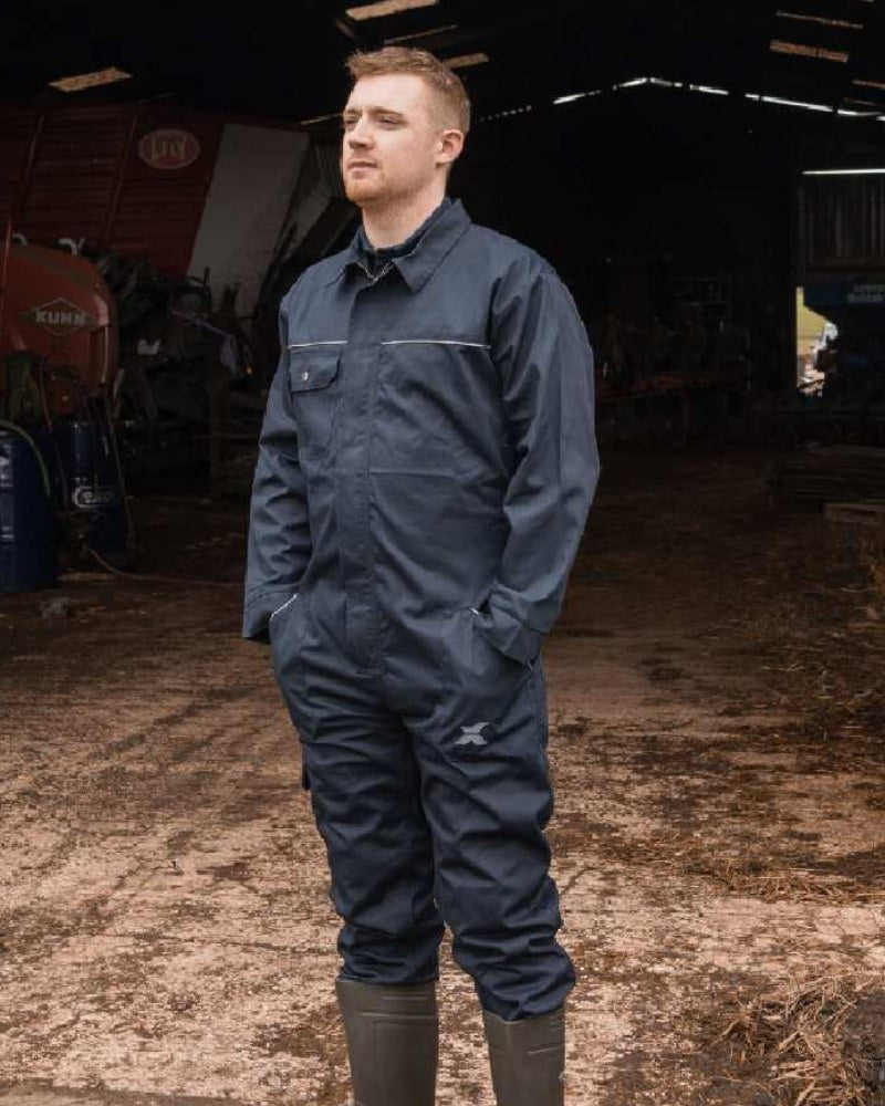 Man wearing Xpert navy work overalls and wellington boots inside a farm building