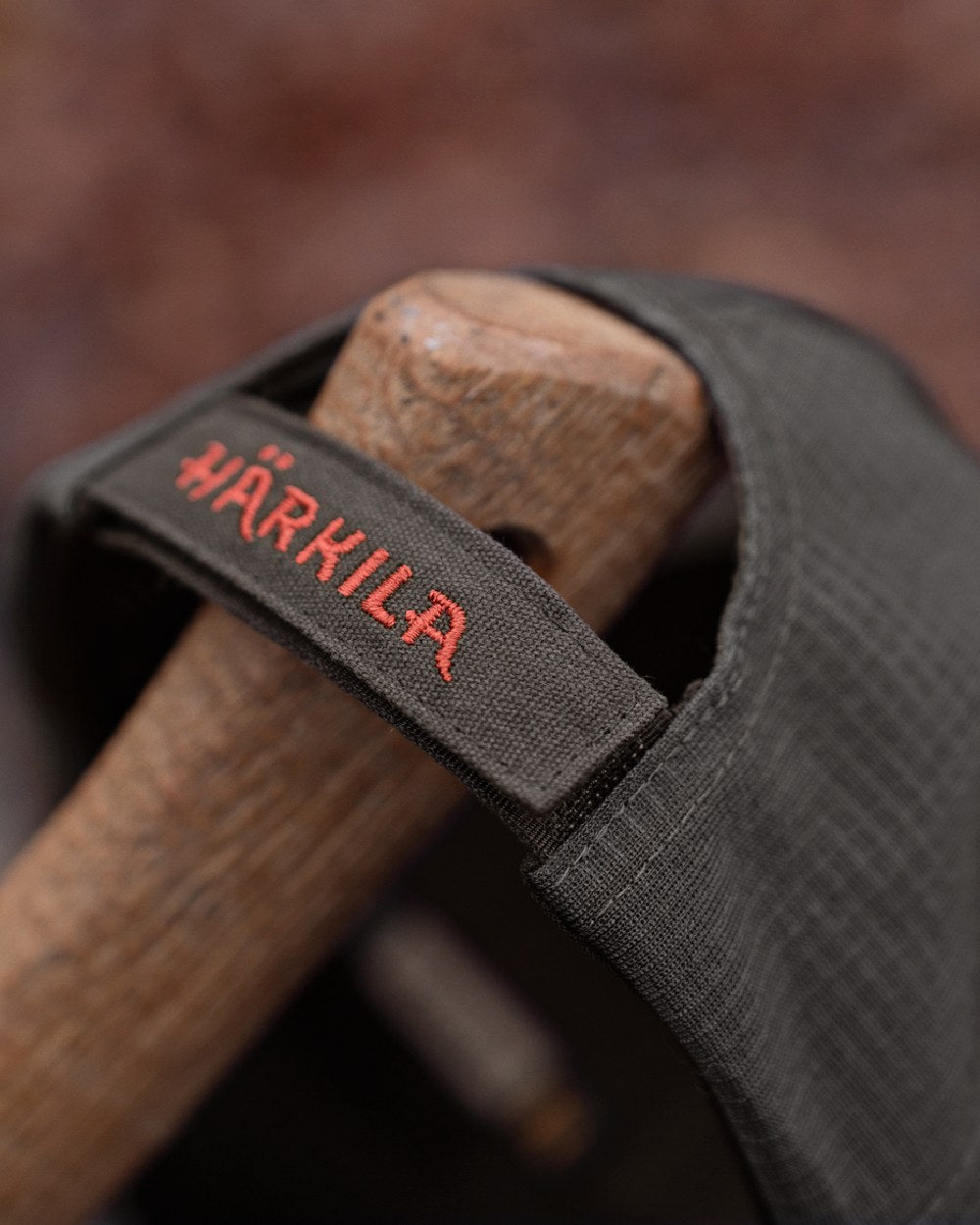 Close-up of a dark gray fabric strap with red embroidered branding, wrapped around a wooden handle. 