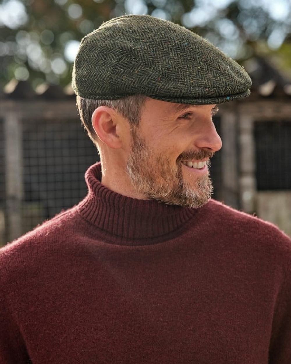 Green Coloured Hoggs of Fife Herringbone Waterproof Tweed Flat Cap on blurry background 