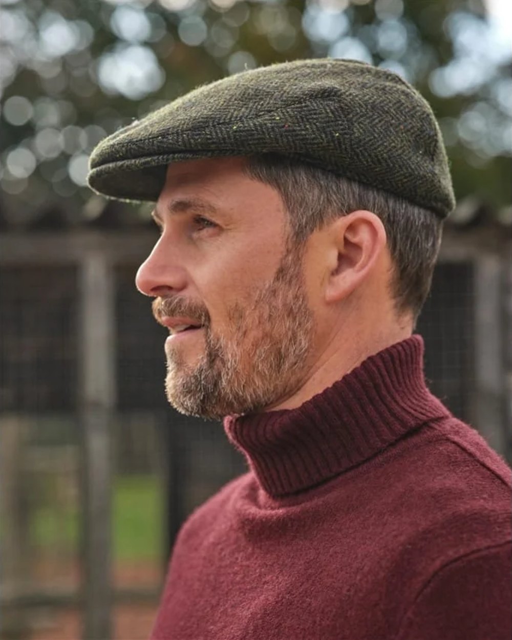 Green Coloured Hoggs of Fife Herringbone Waterproof Tweed Flat Cap on blurry background 