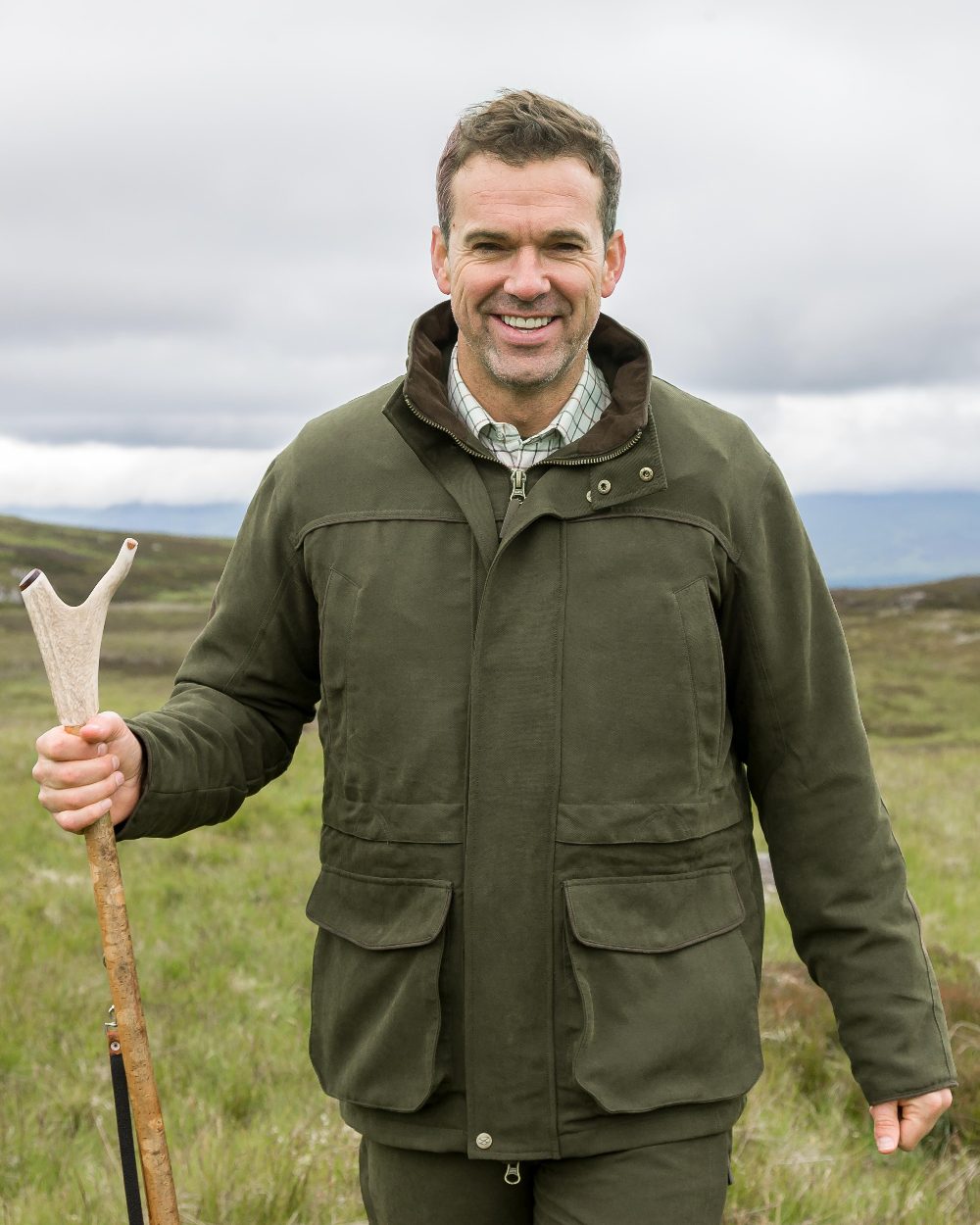 Olive Green Coloured Hoggs of Fife Kincraig Waterproof Field Jacket on countryside background 