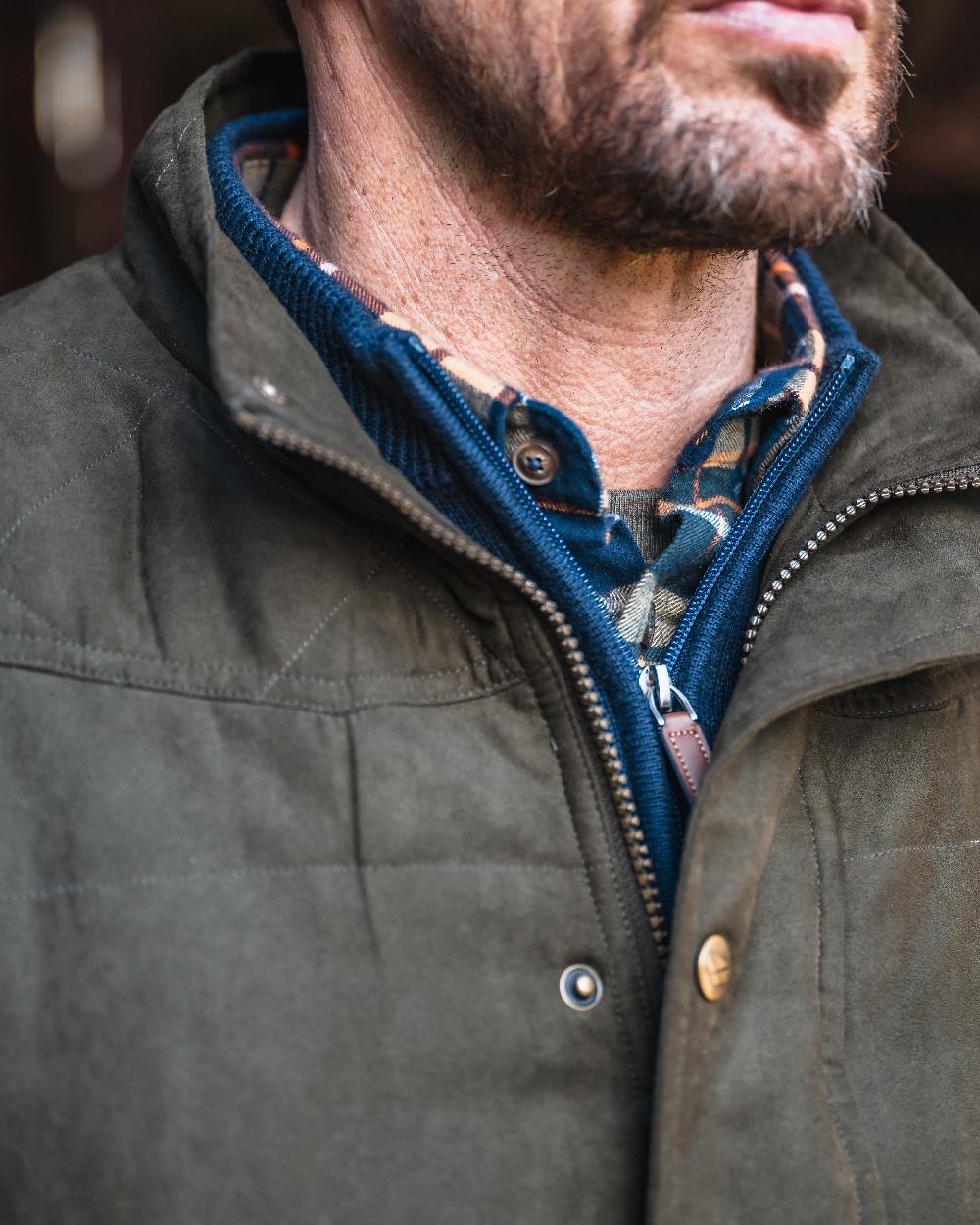 Loden coloured Hoggs of Fife Mens Glenbervie Quilted Gilet on blurry background 