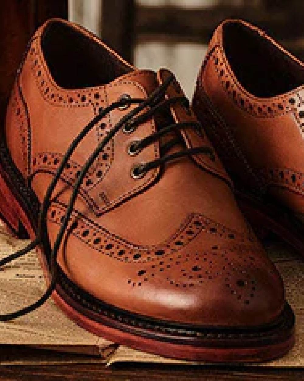 Burnished Tan Coloured Hoggs of Fife Muirfield Brogue Shoe Rubber Soles on wood background 