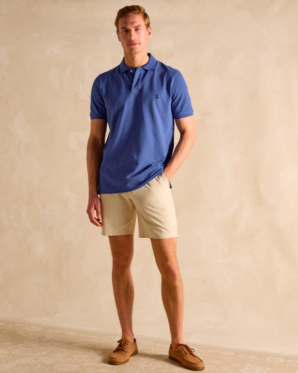 Blue coloured Joules Mens Woody Cotton Pique Polo Shirt on wall background 