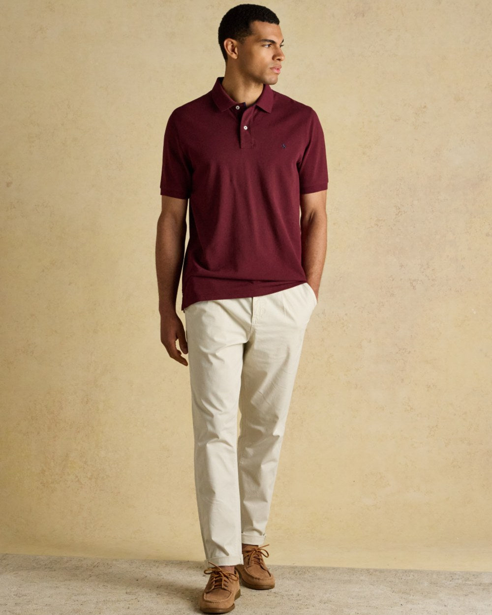 Burgundy coloured Joules Mens Woody Cotton Pique Polo Shirt on wall background 