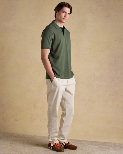 Khaki Green coloured Joules Mens Woody Cotton Pique Polo Shirt on wall background 