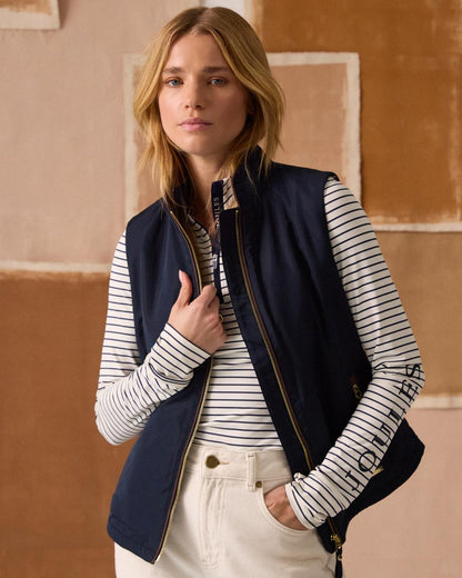 Navy coloured Joules Womens Farnham Fleece Lined Lightweight Gilet on wall background 