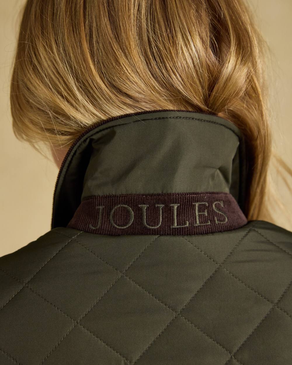 Khaki Green coloured Joules Womens Highgrove Diamond Quilted Jacket on beige background 