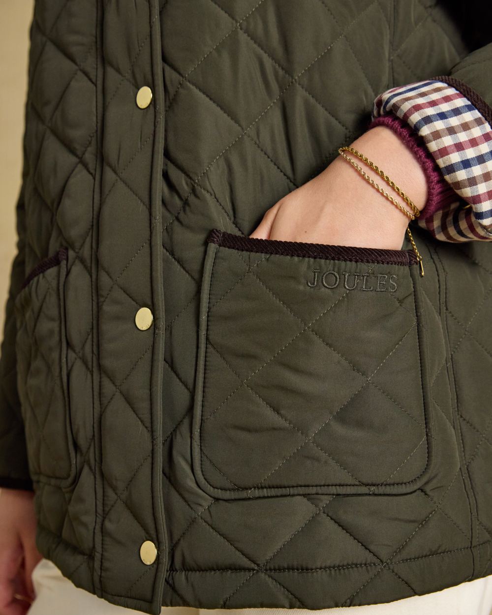 Khaki Green coloured Joules Womens Highgrove Diamond Quilted Jacket on beige background 