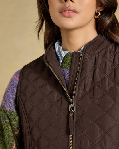 Chocolate Brown Coloured Joules Minx Showerproof Diamond Quilted Gilet on wall background 
