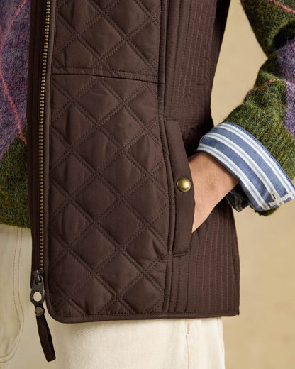 Chocolate Brown Coloured Joules Minx Showerproof Diamond Quilted Gilet on wall background 