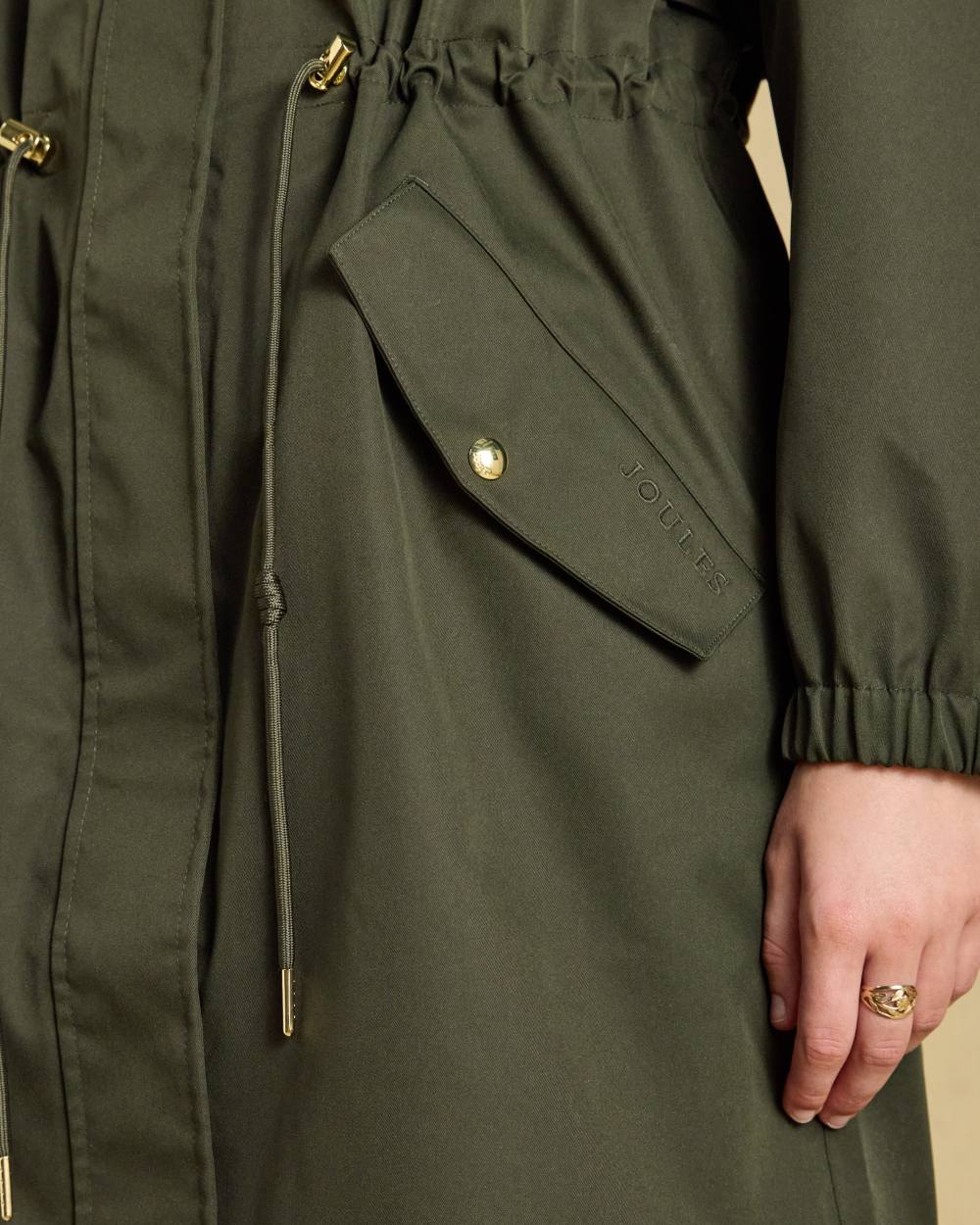 Green coloured Joules Womens Stormwell Waterproof Longline Hooded Raincoat on indoor background 