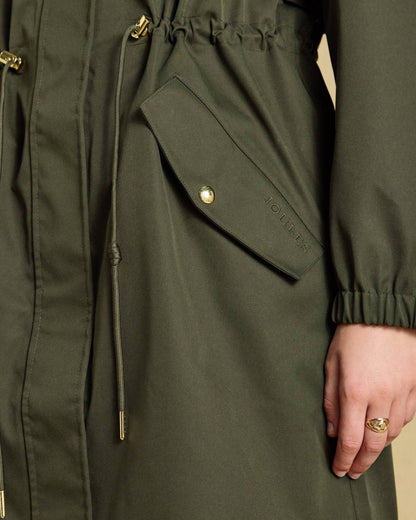 Green coloured Joules Womens Stormwell Waterproof Longline Hooded Raincoat on indoor background 