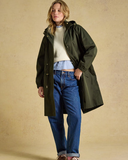 Green coloured Joules Womens Stormwell Waterproof Longline Hooded Raincoat on indoor background 