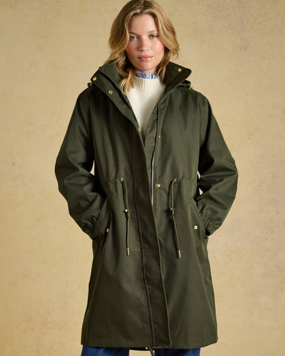 Green coloured Joules Womens Stormwell Waterproof Longline Hooded Raincoat on indoor background 