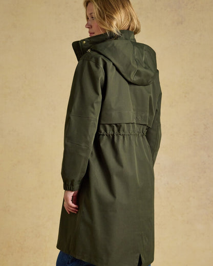 Green coloured Joules Womens Stormwell Waterproof Longline Hooded Raincoat on indoor background 