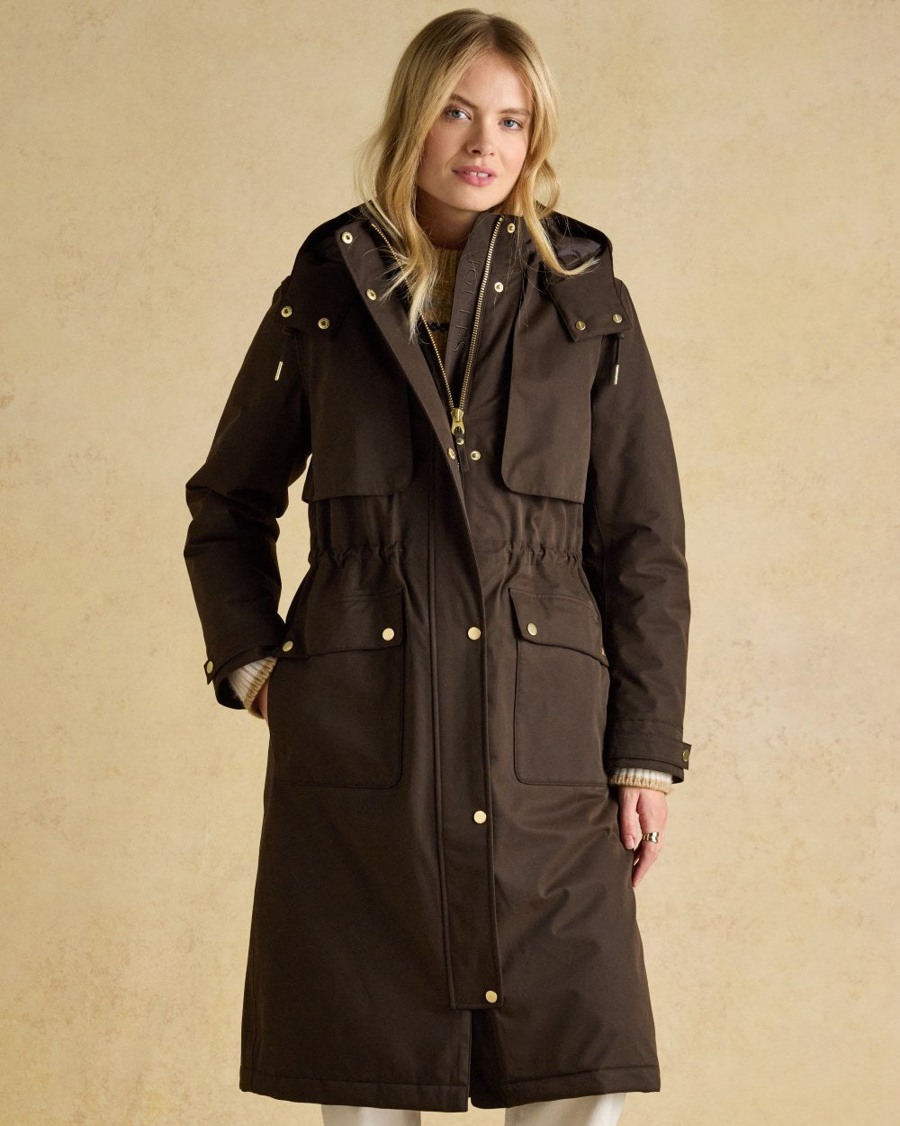 Chocolate Brown coloured Joules Womens Warmwell Waterproof Fleece Lined Raincoat on tan background 