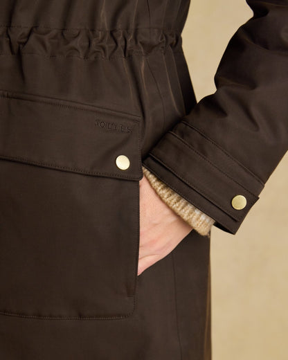 Chocolate Brown coloured Joules Womens Warmwell Waterproof Fleece Lined Raincoat on tan background 