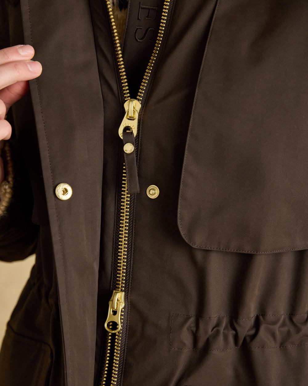 Chocolate Brown coloured Joules Womens Warmwell Waterproof Fleece Lined Raincoat on tan background 