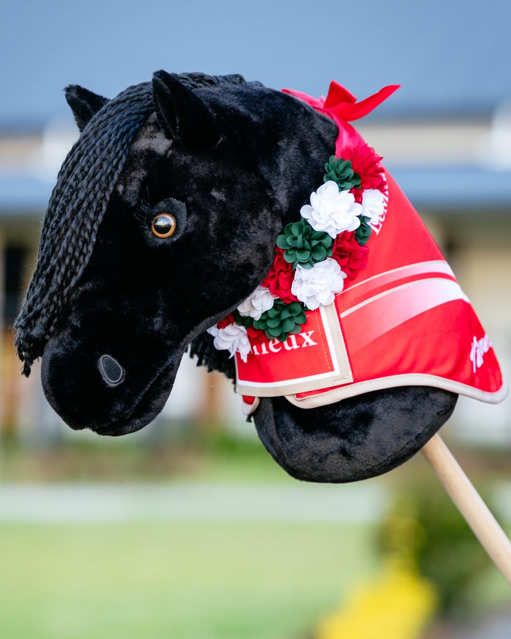 Red coloured LeMieux Hobby Horse Flower Sash on blurry background 