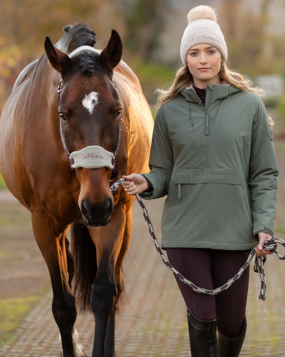 Rosemary coloured LeMieux Phoebe Half Zip Waterproof Anorak on blurry background 