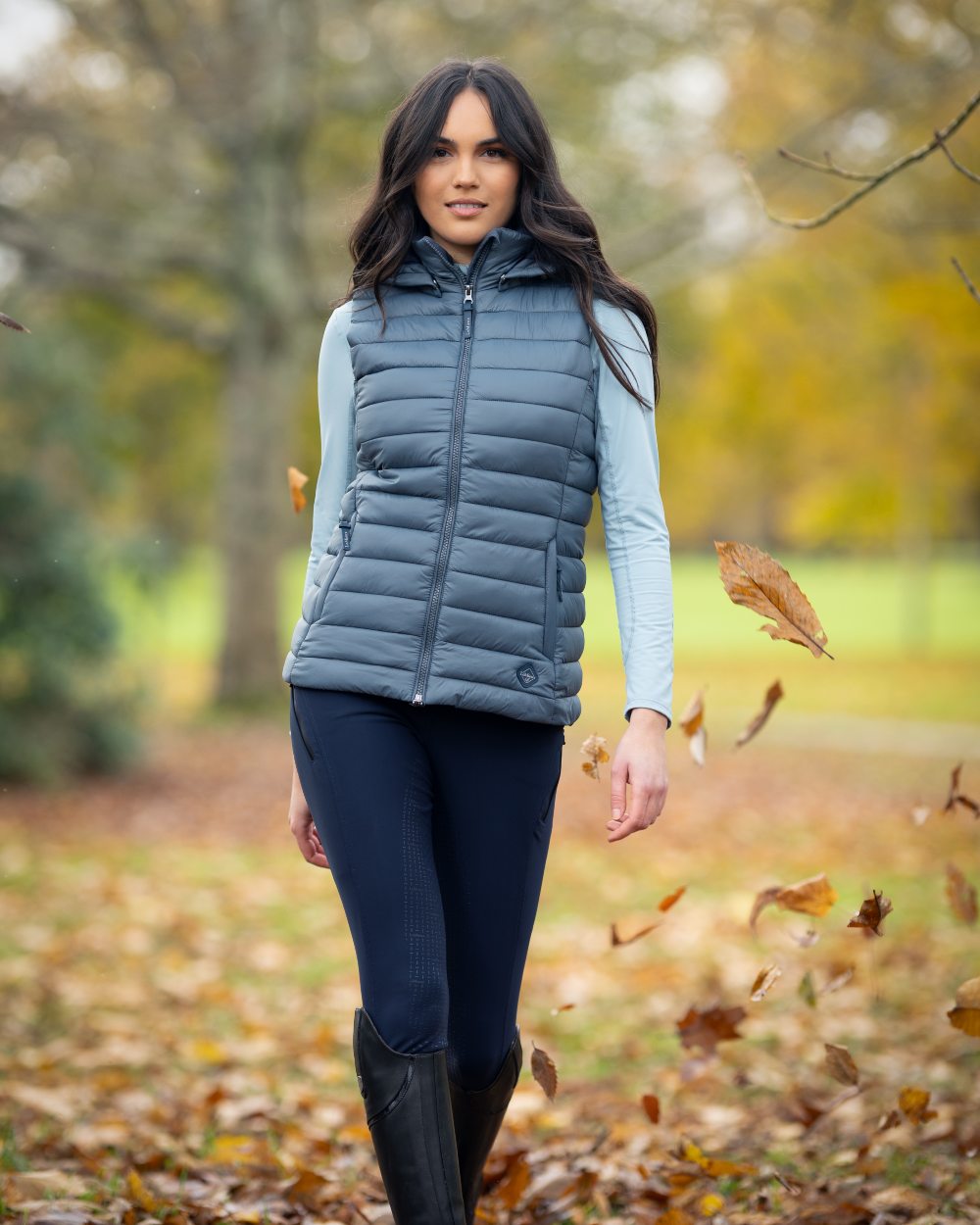 Petrol coloured LeMieux Tilly Hooded Puffer Gilet on blurry park background 