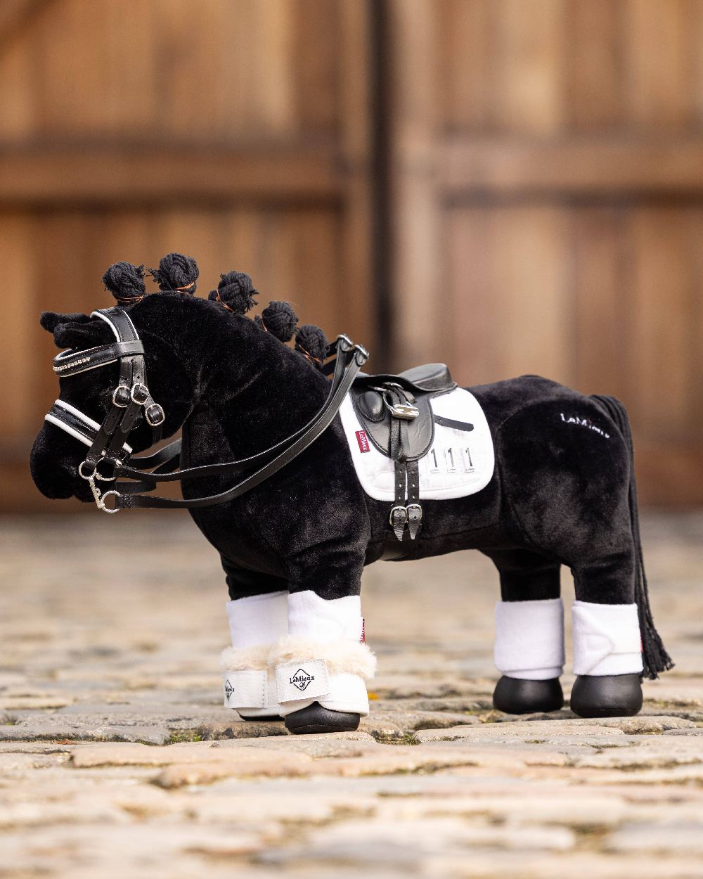 White coloured LeMieux Toy Pony Dressage Over Reach Boot on blurry door background 