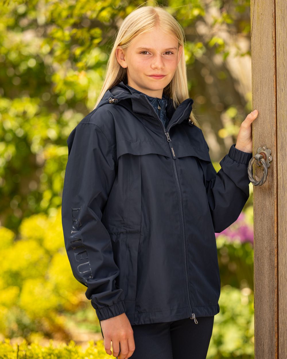 Navy coloured LeMieux Young Rider Dolcie Waterproof Jacket on blurry background 