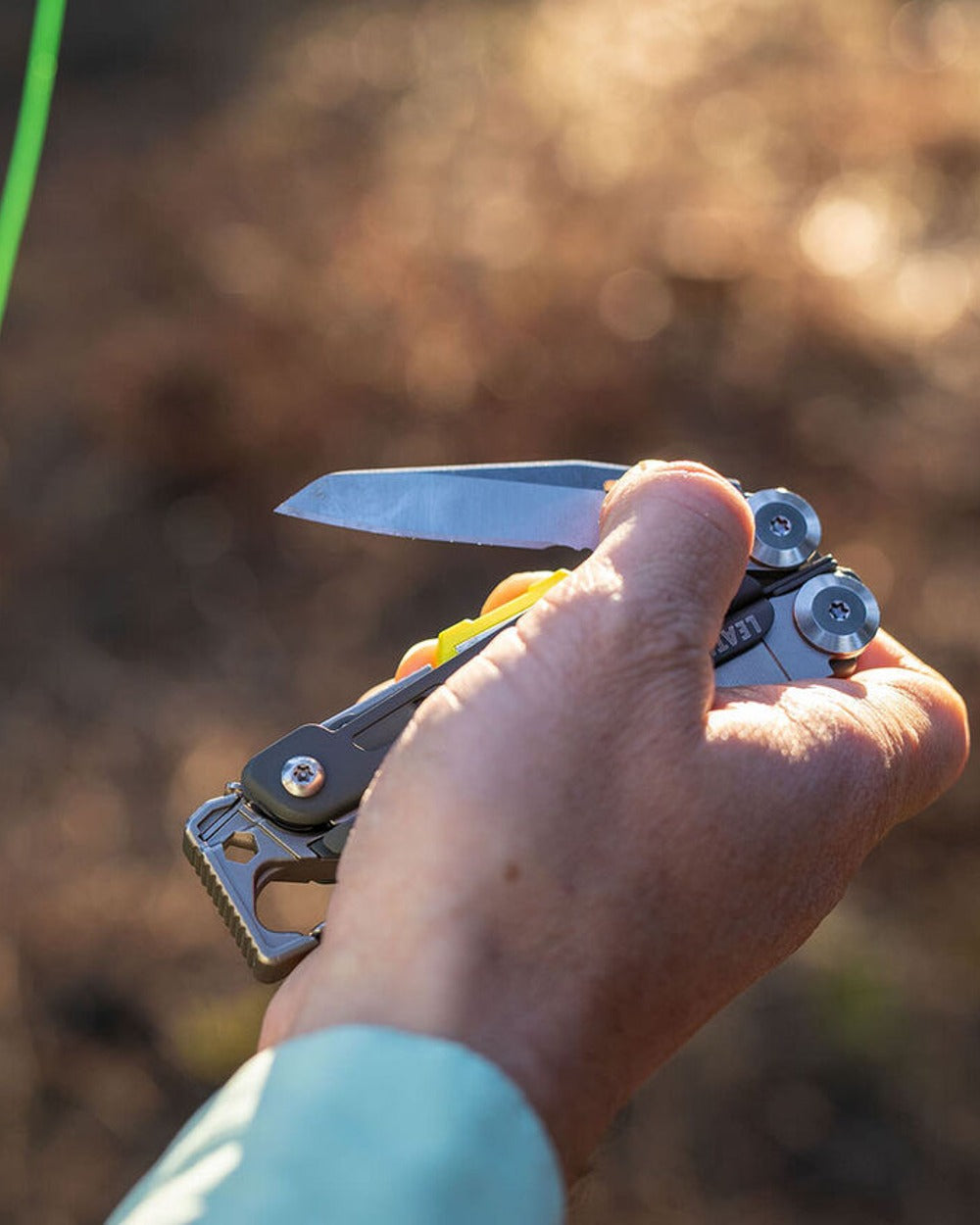 Stainless Steel Coloured Leatherman Signal+ Multi-Tool W/ Nylon Sheath On A Forest Background 