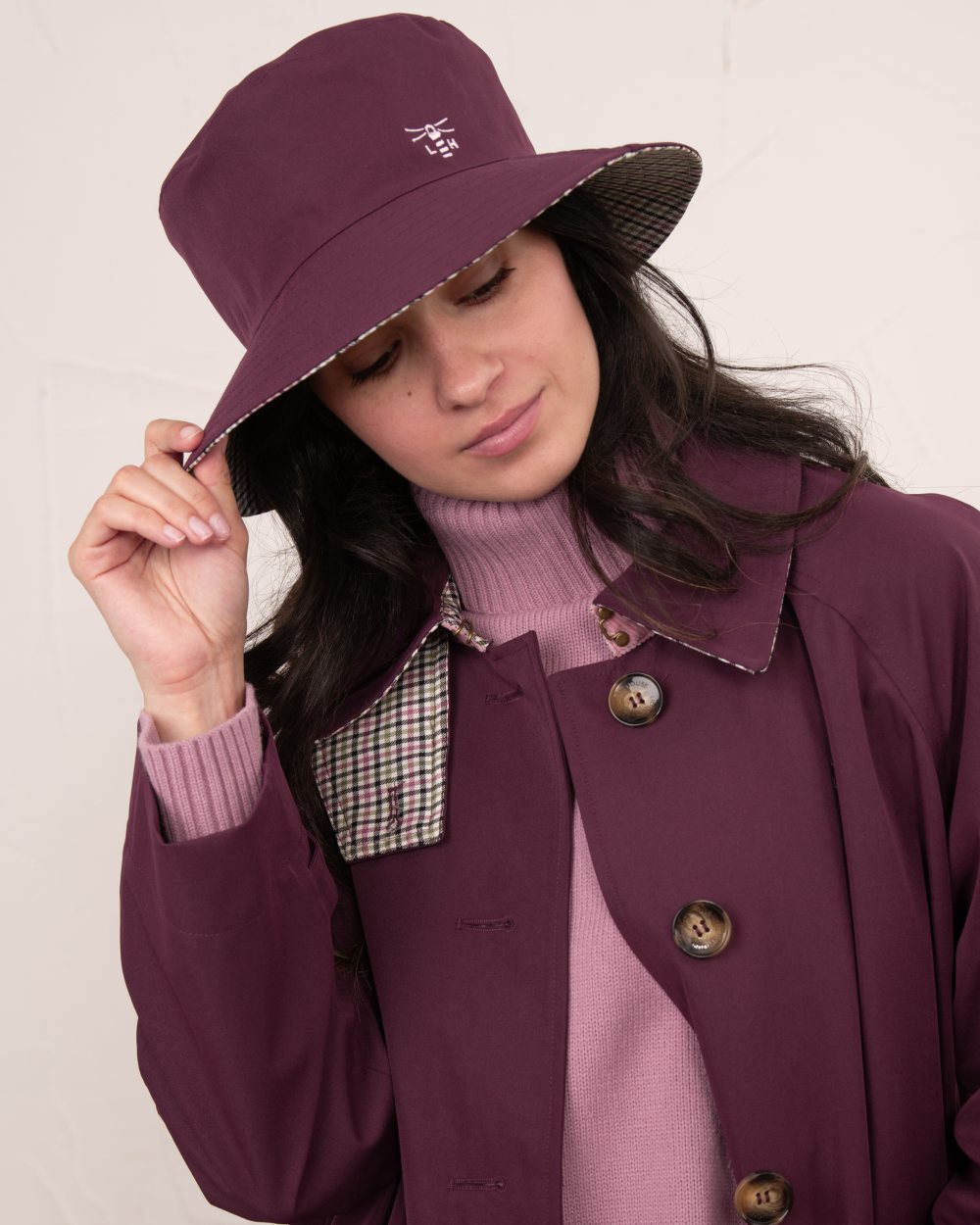 Damson coloured Lighthouse Edie Reversible Rain Hat on wall background 