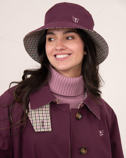 Damson coloured Lighthouse Edie Reversible Rain Hat on wall background 