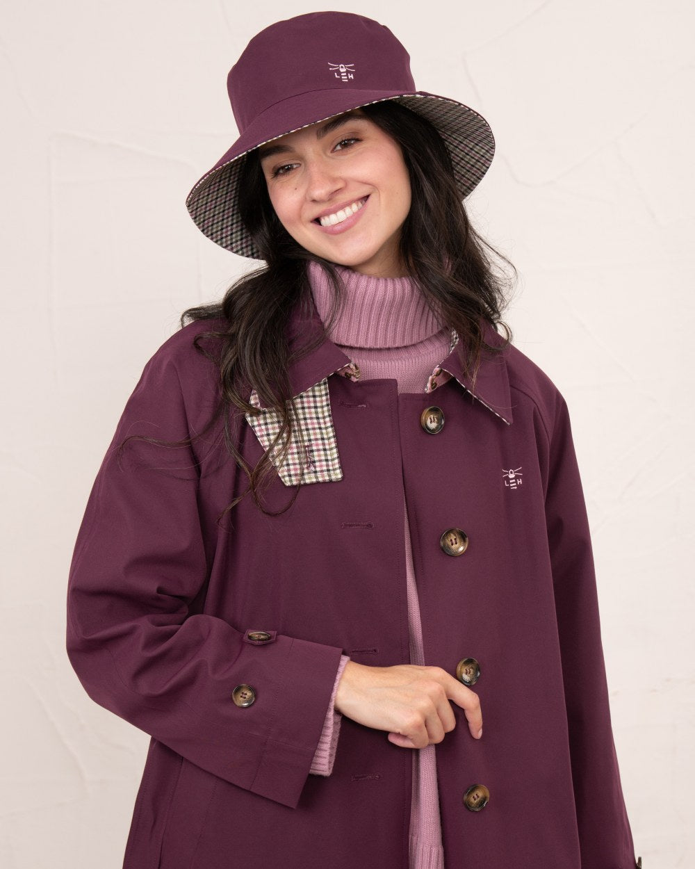 Damson coloured Lighthouse Edie Reversible Rain Hat on wall background 