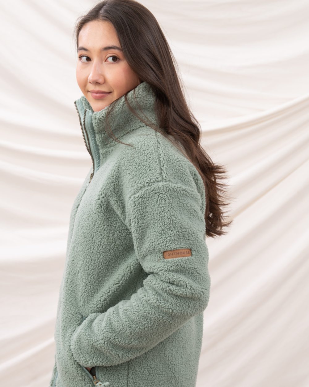 Sage coloured Lighthouse Ladies Cobh Full Zip Fleece Jacket on curtain background 