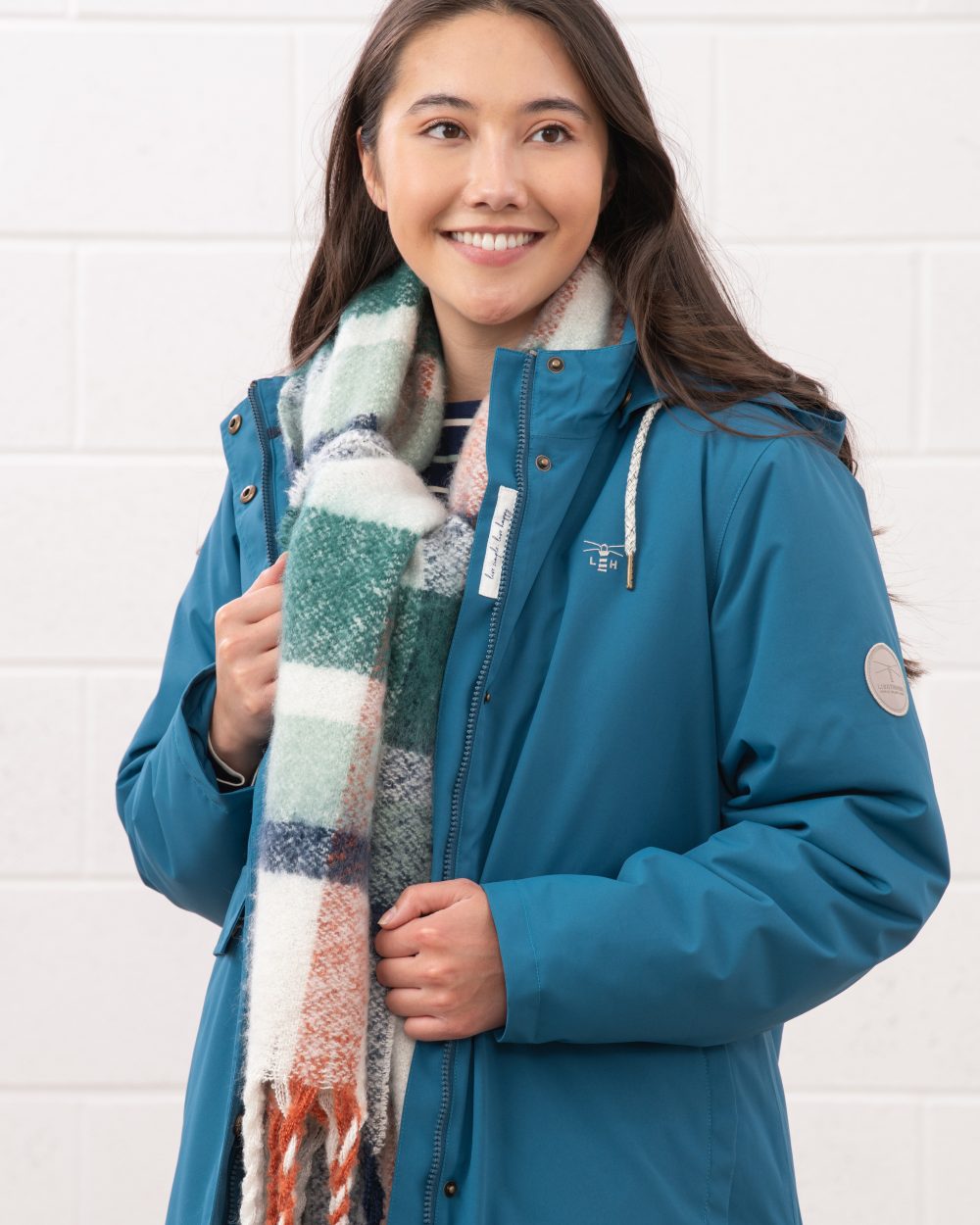 Teal coloured Lighthouse Ladies Tess Coat on wall background 