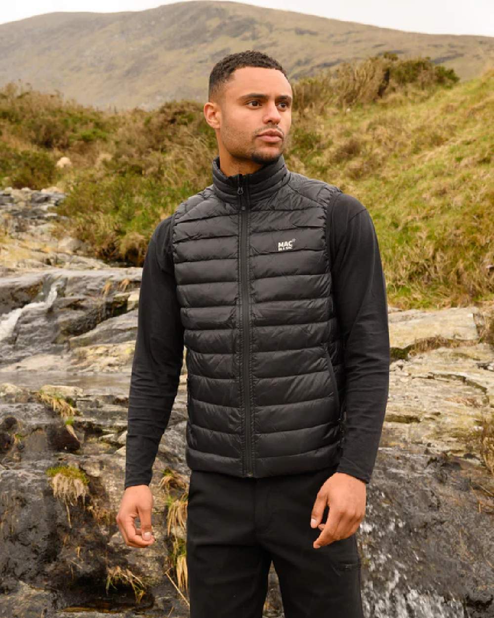 Jet Black coloured Mac In A Sac Mens Alpine Down Gilet on blurry mountain background 