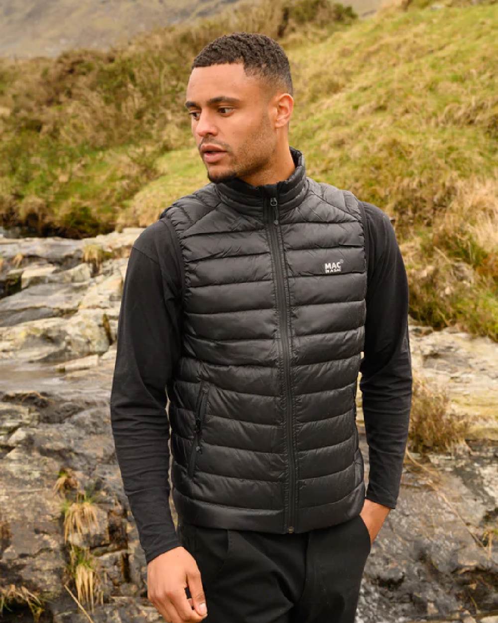 Jet Black coloured Mac In A Sac Mens Alpine Down Gilet on blurry mountain background 