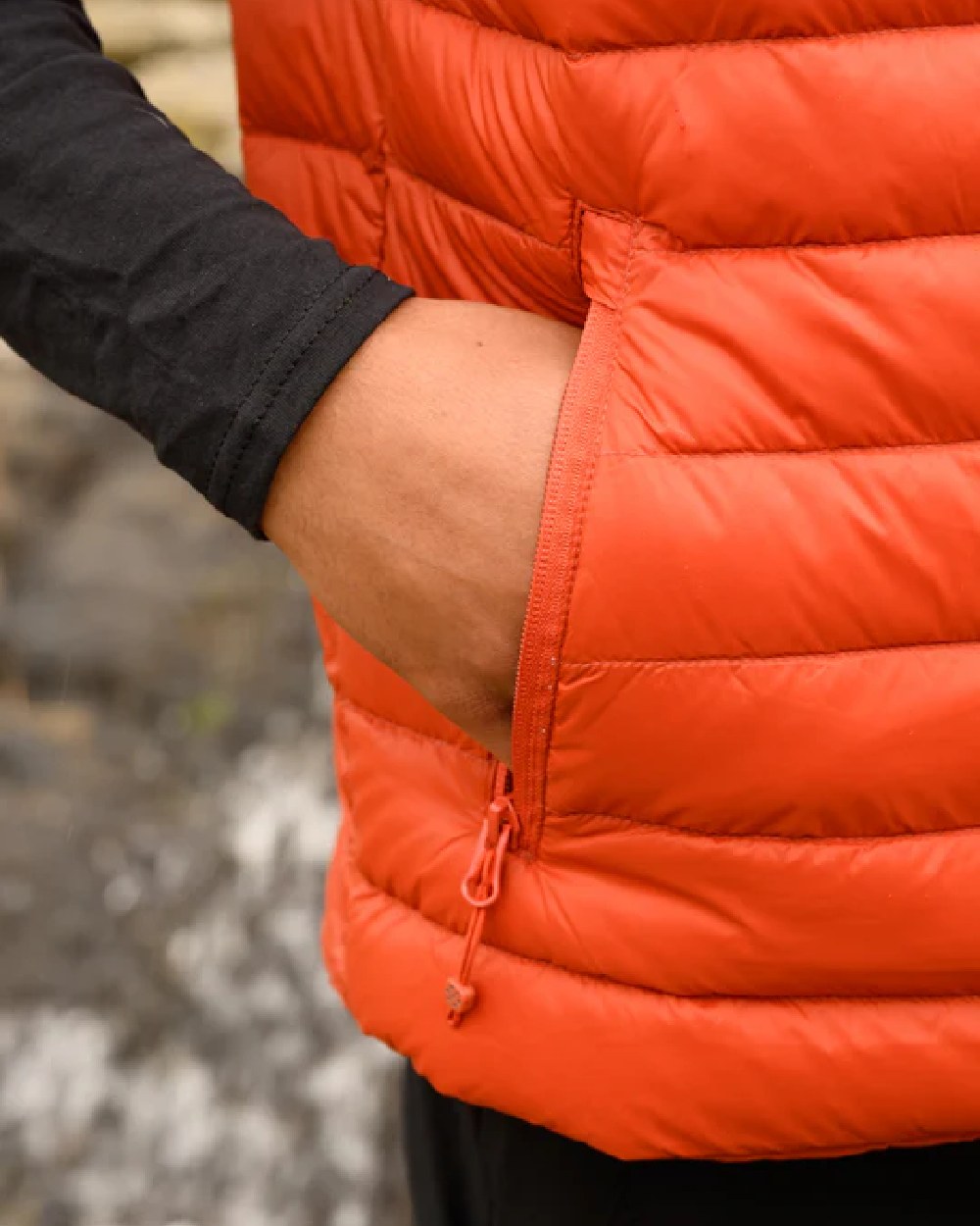 Burnt Orange coloured Mac In A Sac Mens Alpine Down Gilet on blurry mountain background 