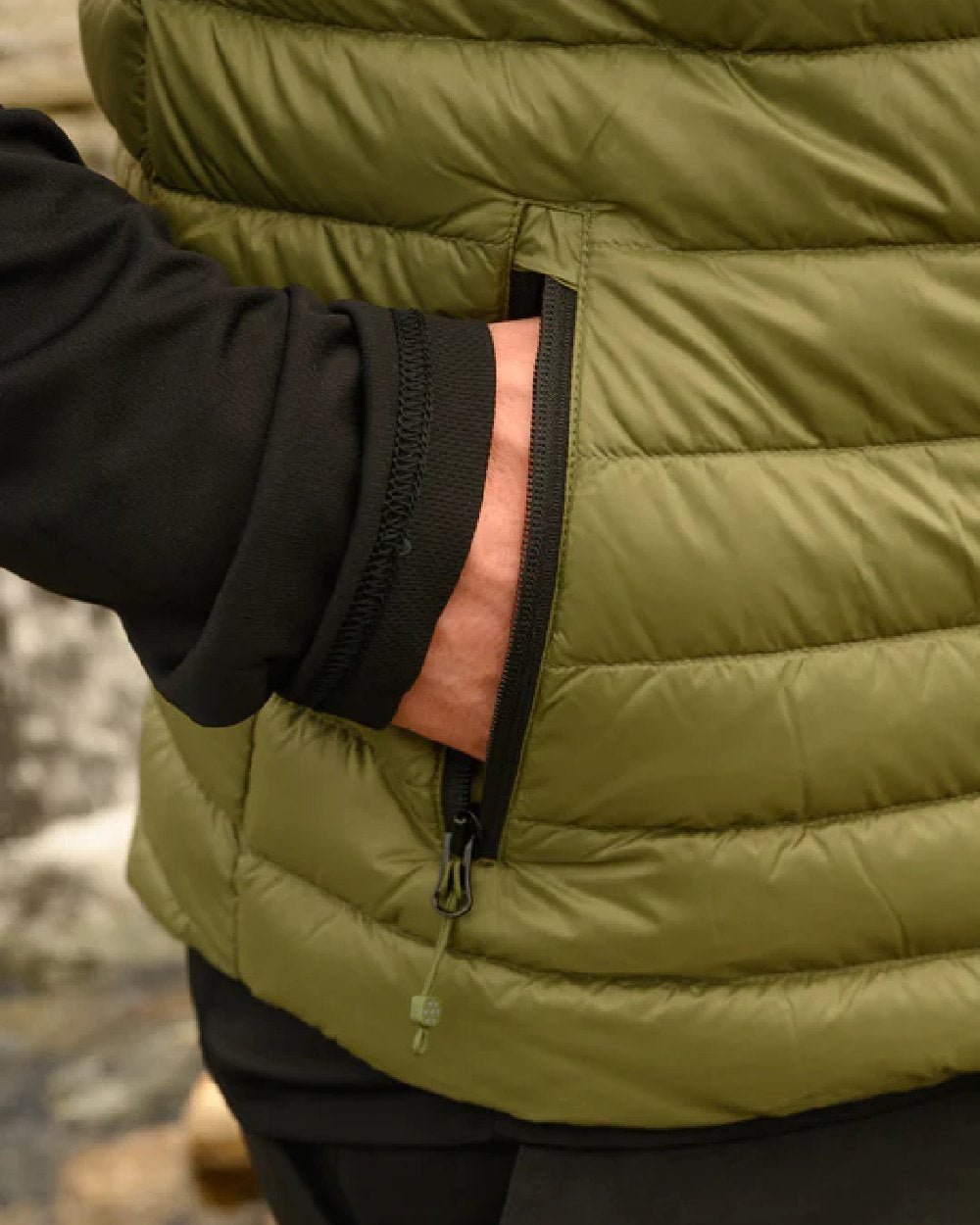 Khaki coloured Mac In A Sac Mens Alpine Down Gilet on blurry mountain background 