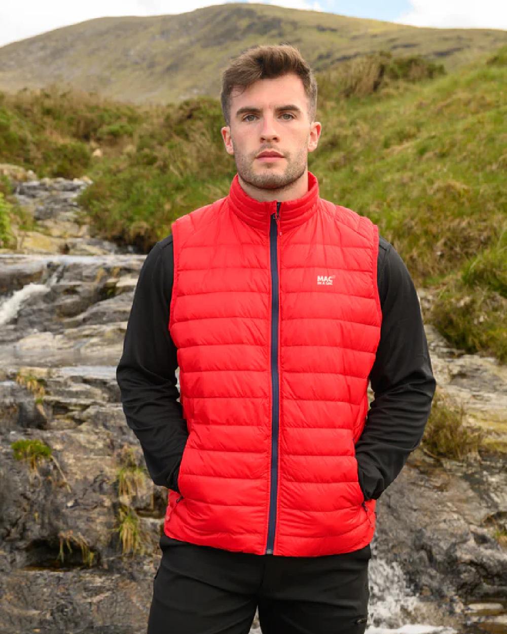 Red coloured Mac In A Sac Mens Alpine Down Gilet on blurry green background 