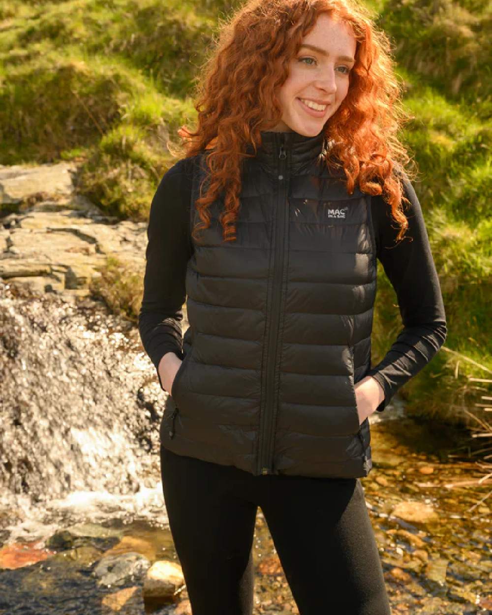 Black coloured Mac In A Sac Alpine Womens Down Gilet on green background 