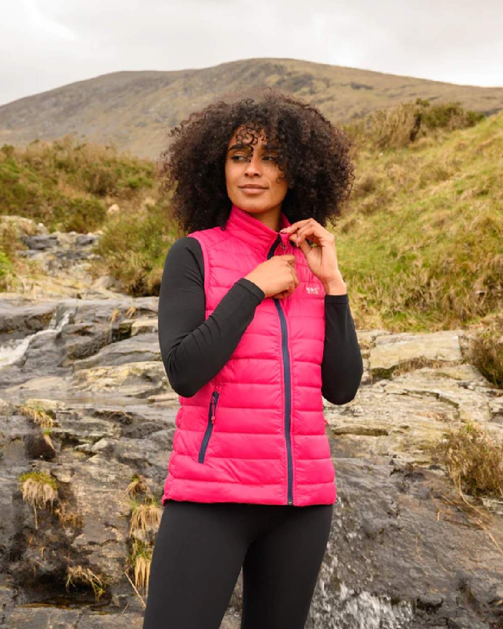 Pink coloured Mac In A Sac Alpine Womens Down Gilet on blurry background 