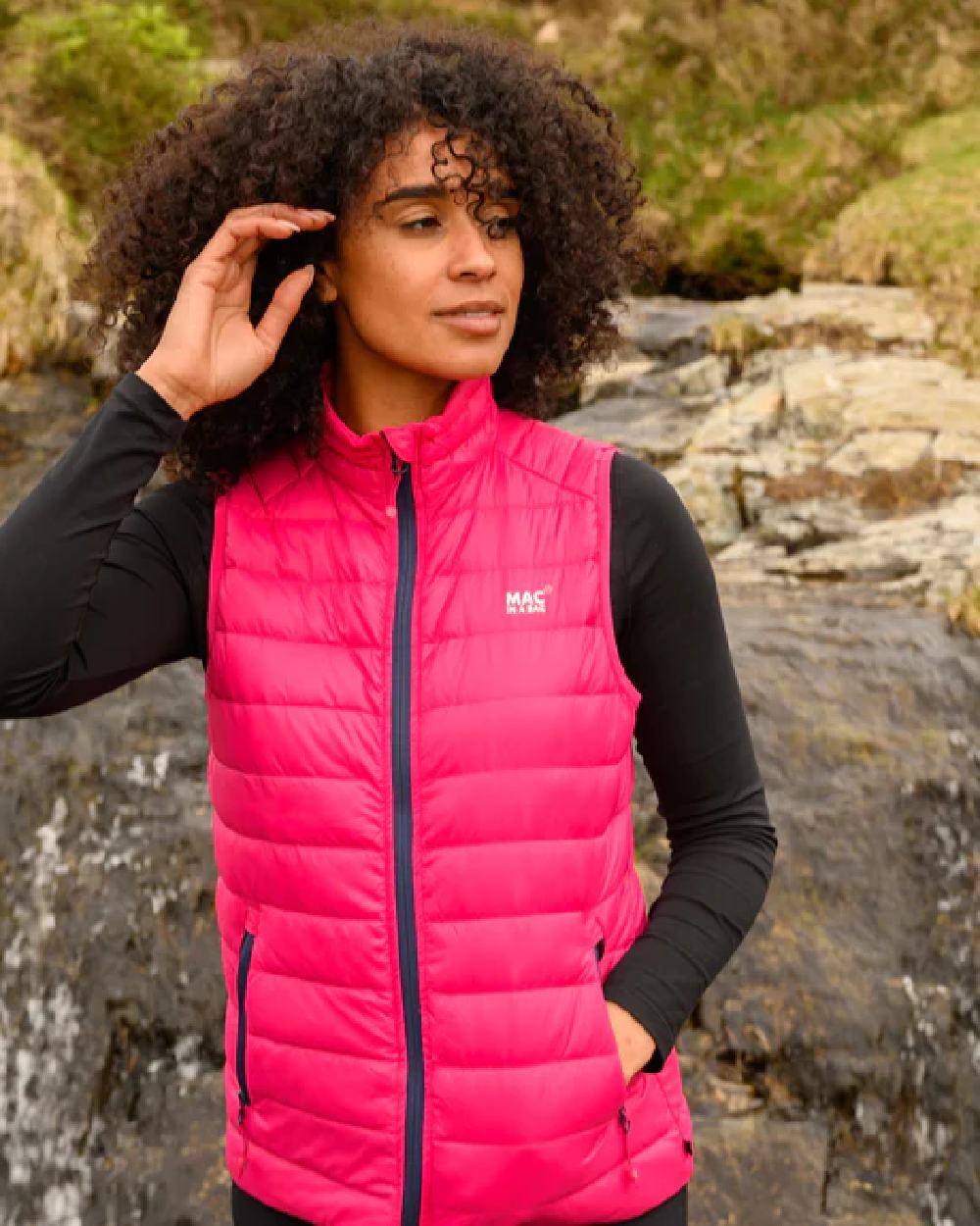 Pink coloured Mac In A Sac Alpine Womens Down Gilet on blurry background 