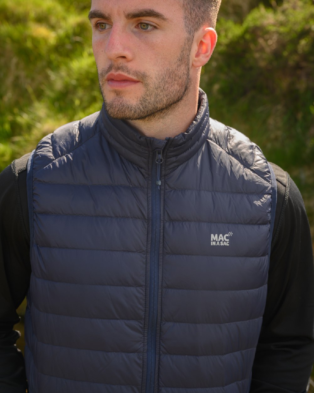 Navy Coloured Mac In A Sac Mens Alpine Down Gilet on blurry background 